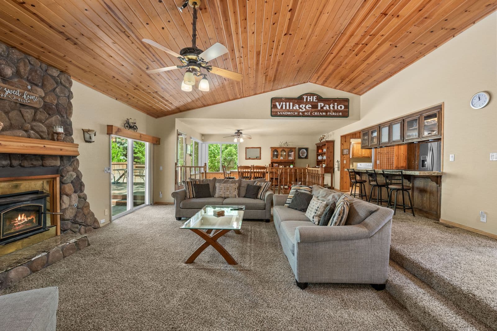 Ikoi Homes living room with a stone fireplace, vaulted wood ceiling, and open kitchen