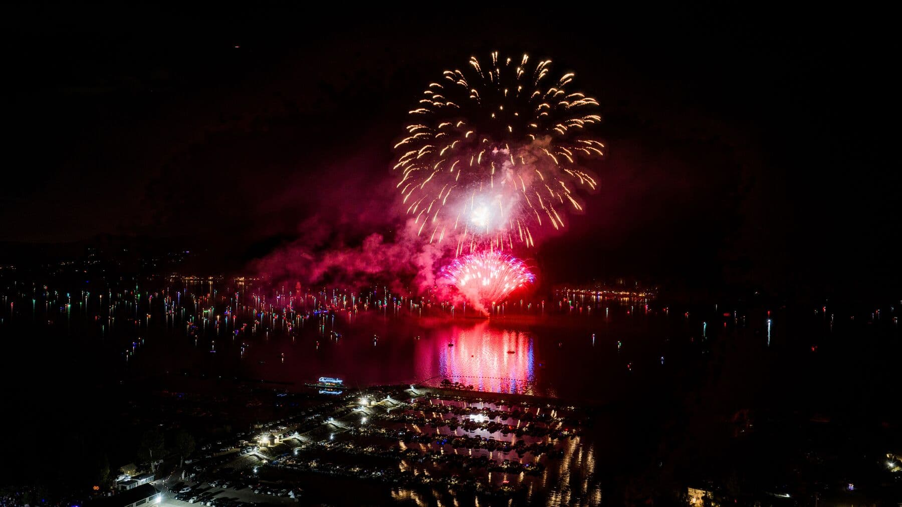 Fireworks over the lake with boats lit on the water
